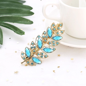 Close-up of golden leaf hair clip with sky blue crystals on elegant white mesh background