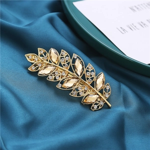 Elegant gold leaf-shaped hair clip with champagne crystals on dark blue silk background