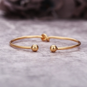 Détail d'un bracelet jonc doré minimaliste avec un nœud et des extrémités sphériques