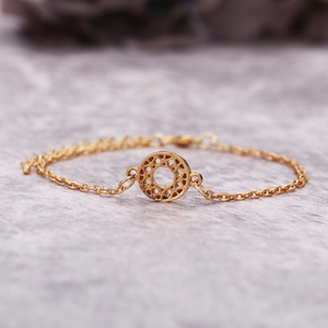 Gros plan d'un bracelet doré avec un pendentif circulaire aux motifs géométriques ajourés