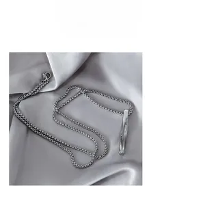 Detail shot of silver twisted rectangular pendant on chain against grey silk background