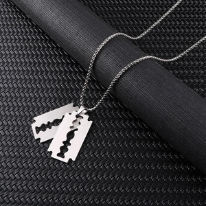 Close-up of matte silver razor blade pendants with a ball chain on industrial background