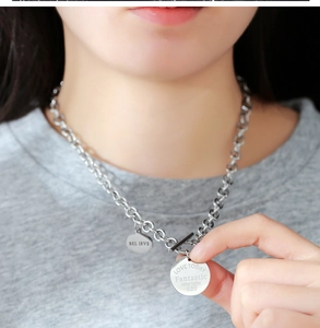 Détail du fermoir OT et des pendentifs ronds gravés sur un collier à chaîne épaisse