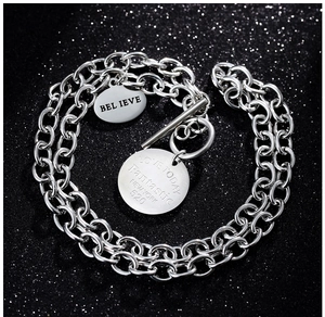 Détail d'un collier chaîne épaisse en acier argenté avec fermoir T et pendentifs gravés