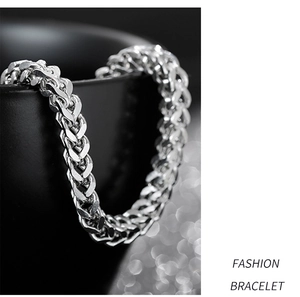 Macro shot of silver stainless steel wheat chain bracelet draped over a black cup