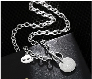 Gros plan du collier à fermoir OT argenté avec pendentifs gravés sur une boîte noire