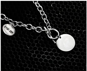 Détail macro de la chaîne en acier avec pendentif BELIEVE et médaillon blanc rond