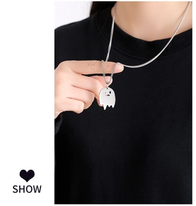 Close-up of a silver ghost pendant necklace held by a hand over a dark background