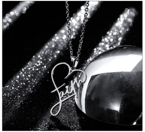 Macro detail of silver heart necklace with Faith engraving on black background