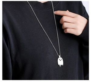 Detail of a silver ghost pendant necklace styled over a black sweater for Halloween