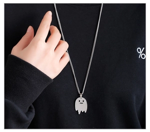 Detail of silver ghost pendant on a long chain worn over a black knitted sweater