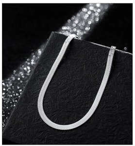 Detailed close-up of a silver flat snake bone chain with metallic luster on black box
