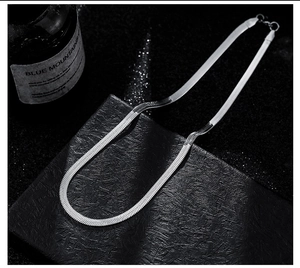 Close-up of a silver flat herringbone chain necklace on a black textured background