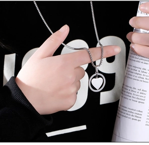 Close-up of a silver heart pendant necklace on a black sweatshirt in a street style scene