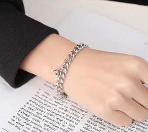 Close-up of silver Cuban chain bracelet with heart charm on wrist over magazine
