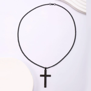 Flat lay of minimalist matte black stainless steel cross pendant on a white textured board