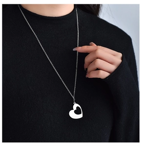 Vue détaillée d'un collier cœur évidé argenté porté sur un pull noir contrasté
