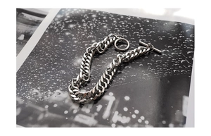 Close-up of silver Cuban link bracelet with a decorative OT toggle clasp detail