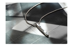 Macro shot of minimalist polished stainless steel bar pendant on geometric background