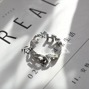 Bague en acier titane argenté à lettres évidées sur fond de magazine moderne