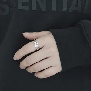 Bague ajourée en acier inoxydable avec lettres argentées portée au doigt