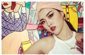 Detail of a golden dumbbell pendant necklace and ball earrings on a model with a pink headband