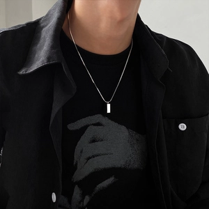 Gros plan d'un collier pendentif rectangulaire argenté minimaliste sur une tenue noire