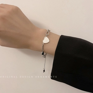 Detail of silver heart charm bracelet worn on wrist showing the intricate chain and toggle