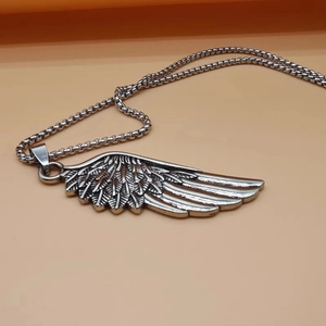 Gros plan du collier pendentif aile argentée avec détails de plumes sur fond rose