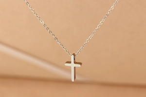 Macro shot of a minimalist silver titanium steel cross pendant necklace on a warm background