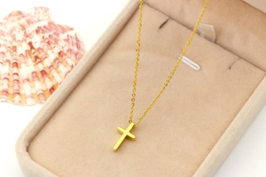 Close-up of golden titanium steel mini cross pendant on chain in beige velvet jewelry box
