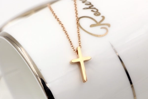 Close-up of polished rose gold cross pendant necklace on a white ceramic cup