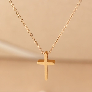 Macro view of gold cross pendant showing brushed metal texture on a fine link chain