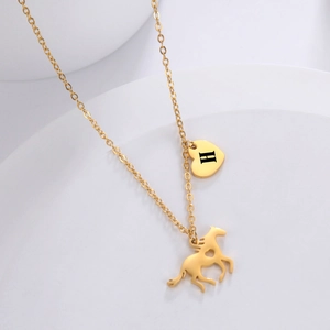 Detailed close-up of gold horse pendant and heart charm with H engraving on fine chain