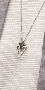 Macro shot of silver stainless steel necklace with double triangle pendant on striped fabric
