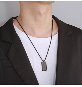 Close-up of a man wearing a minimalist black rectangular dog tag pendant on a slim chain