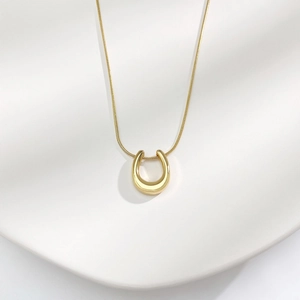 Macro shot of gold U-shaped pendant with a sleek snake chain on a wavy texture