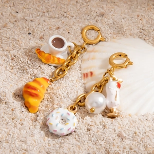 Golden keychain charms with mini coffee cup, donuts and croissant on white beach sand