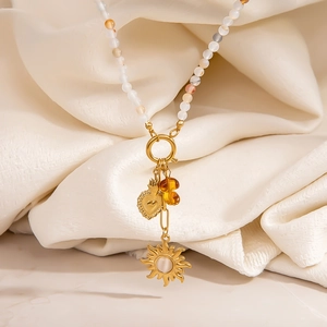 Boho DIY kralenketting met gouden hart hanger en zon charme op beige stoffen
