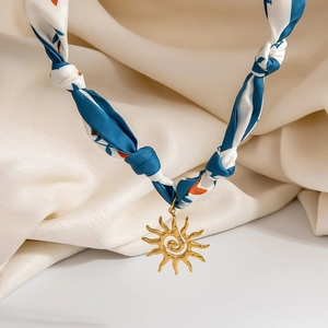 Detail of blue and white printed silk scarf necklace with a golden sun charm pendant