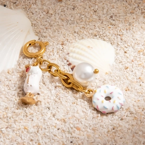 Gold stainless steel charm with enamel donut, cocktail cup and pearl on beach sand