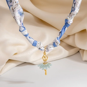 Macro view of golden ballerina pendant on blue floral fabric necklace and silk background