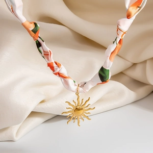 Detailed close-up of a silk scarf necklace with a golden sun pendant on satin background