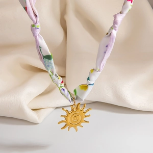 Dettaglio del ciondolo a sole dorato con trama a spirale su una collana di seta a fiori