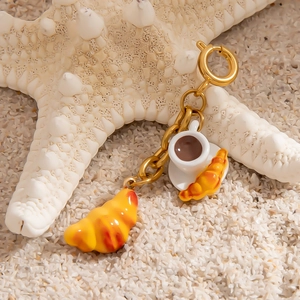 Detailed close-up of golden keychain featuring miniature croissant and coffee cup charms