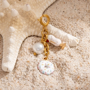 Golden keychain with pearl, enamel donut and wine glass charms on a beach sand background