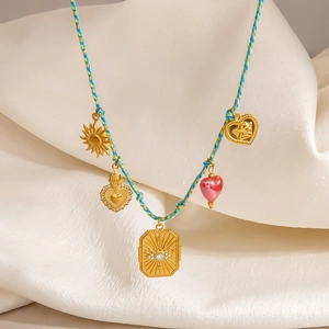 Detail einer Boho-Webkette mit Sonnen-, Herz- und Augen-Anhängern auf weißem Stoff