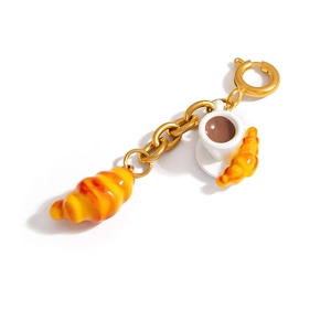 Detail of croissant and coffee pendants with gold metal chain on a white background