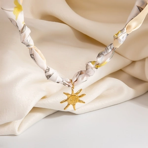 Detailed shot of golden sun face pendant on floral silk scarf necklace with intricate engraving