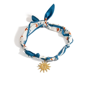 Close-up of silk floral scarf necklace with a golden sun pendant and blue patterns